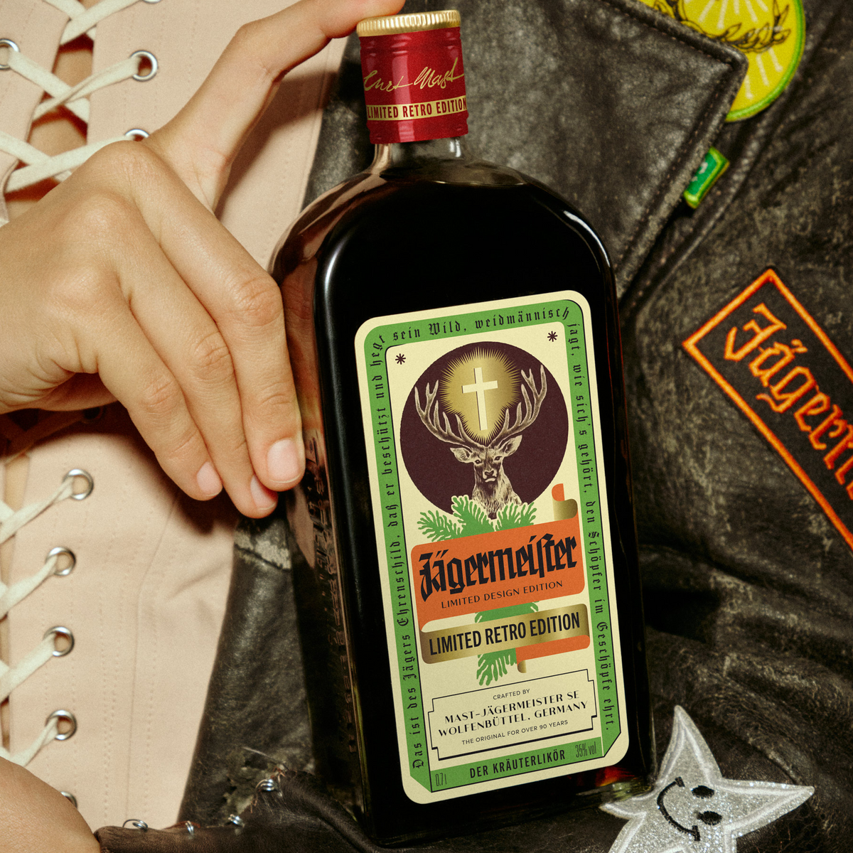A Person wearing a Jägermeister leather jacket presents a close up of the Jägermeister retro bottle.