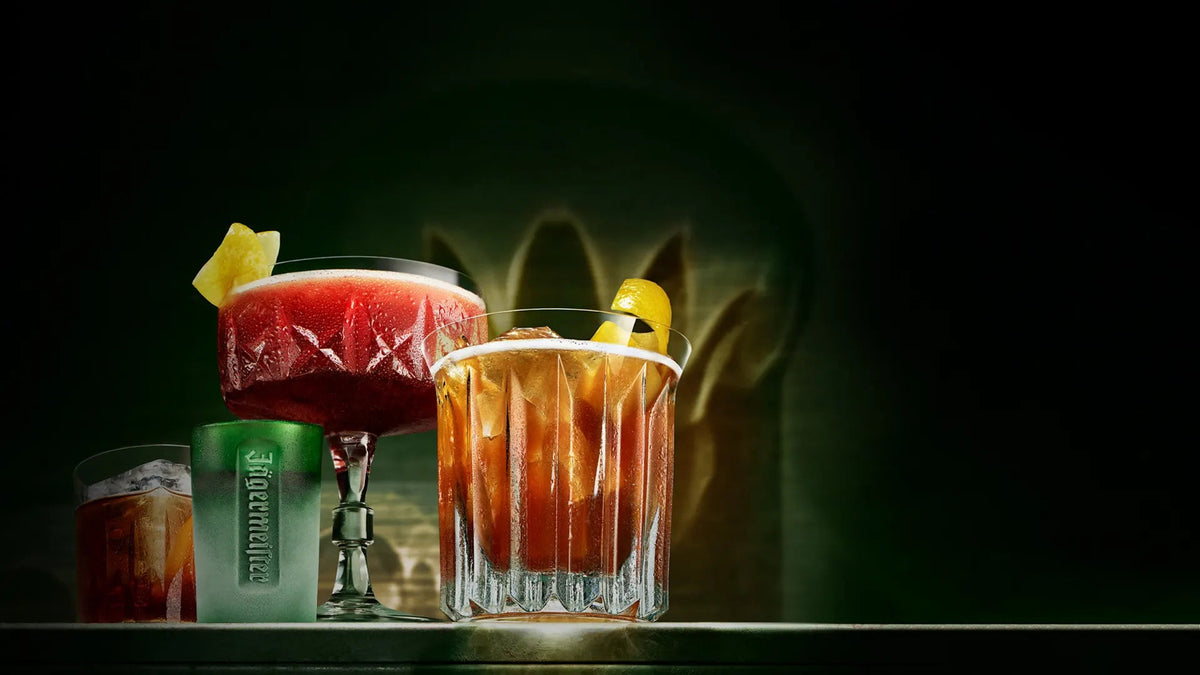 Premium cocktail assortment with a Jägermeister shot glass, citrus garnishes, and dramatic green backlighting.