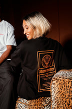 Person wearing a black Jägermeister label t-shirt, sitting against a dark background.