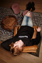 Personne allongée sur un fauteuil en cuir, les pieds posés sur un tapis, portant un sweat-shirt noir Jägermeister.