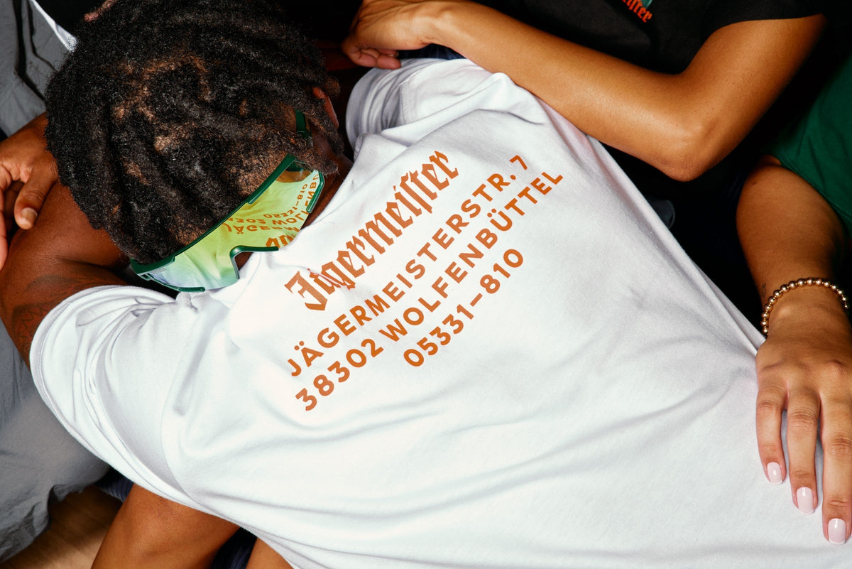 Person wearing a white Jägermeister shirt with orange text on it.