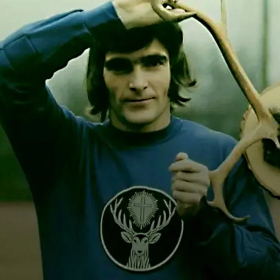 Two men outdoors holding deer antlers above their heads, wearing matching long-sleeve shirts with a black deer head logo. One shirt is blue and the other is yellow.