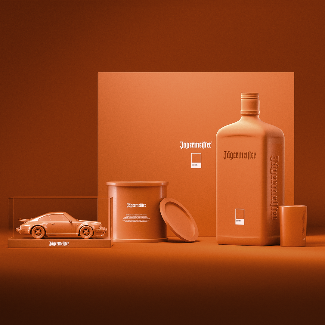 Monochromatic orange display featuring a Jägermeister bottle, model car, container, and cylindrical object arranged against a matching orange background in a stylized product showcase.