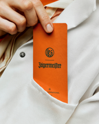 Jägermeister et Kuumba sur une carte parfumée orange tenue par une main sur fond de blouse blanche