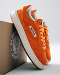 Orange Jägermeister sneakers with white soles and a white side label reading 'Jägermeister', displayed with a brown box printed with 'Flower Society' on a light gray background.