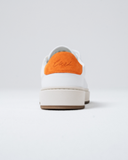 A white Jägermeister sneaker shown from the rear, featuring a vibrant orange suede heel tab with the sneaker name 'Curt' embroidered in brown, a thick off-white midsole, and a brown outsole.